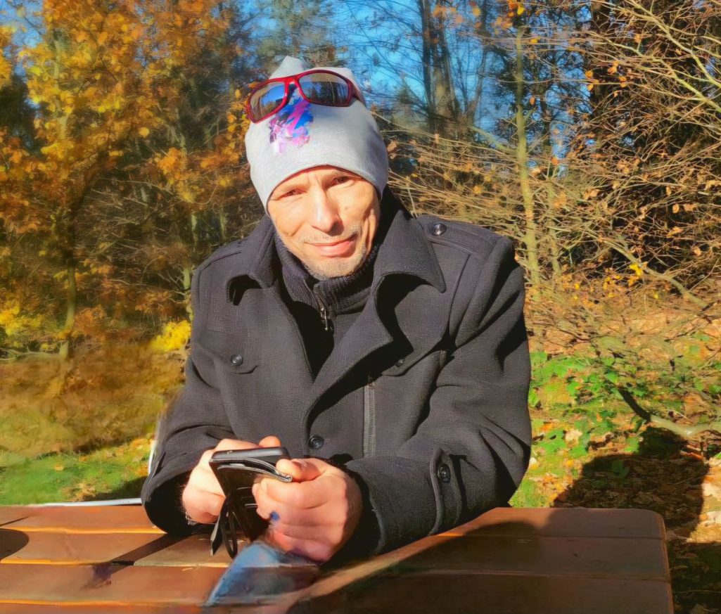 Offline und online Mann in warmer Kleidung sitzt im Freien und hält ein Smartphone in der Hand.